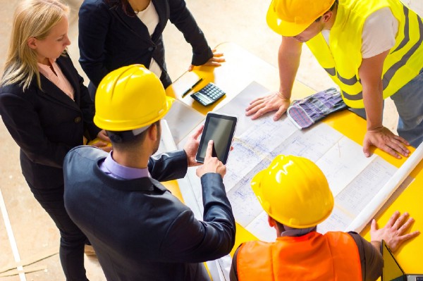 Group of engineers in safety helmets reviewing plans on table